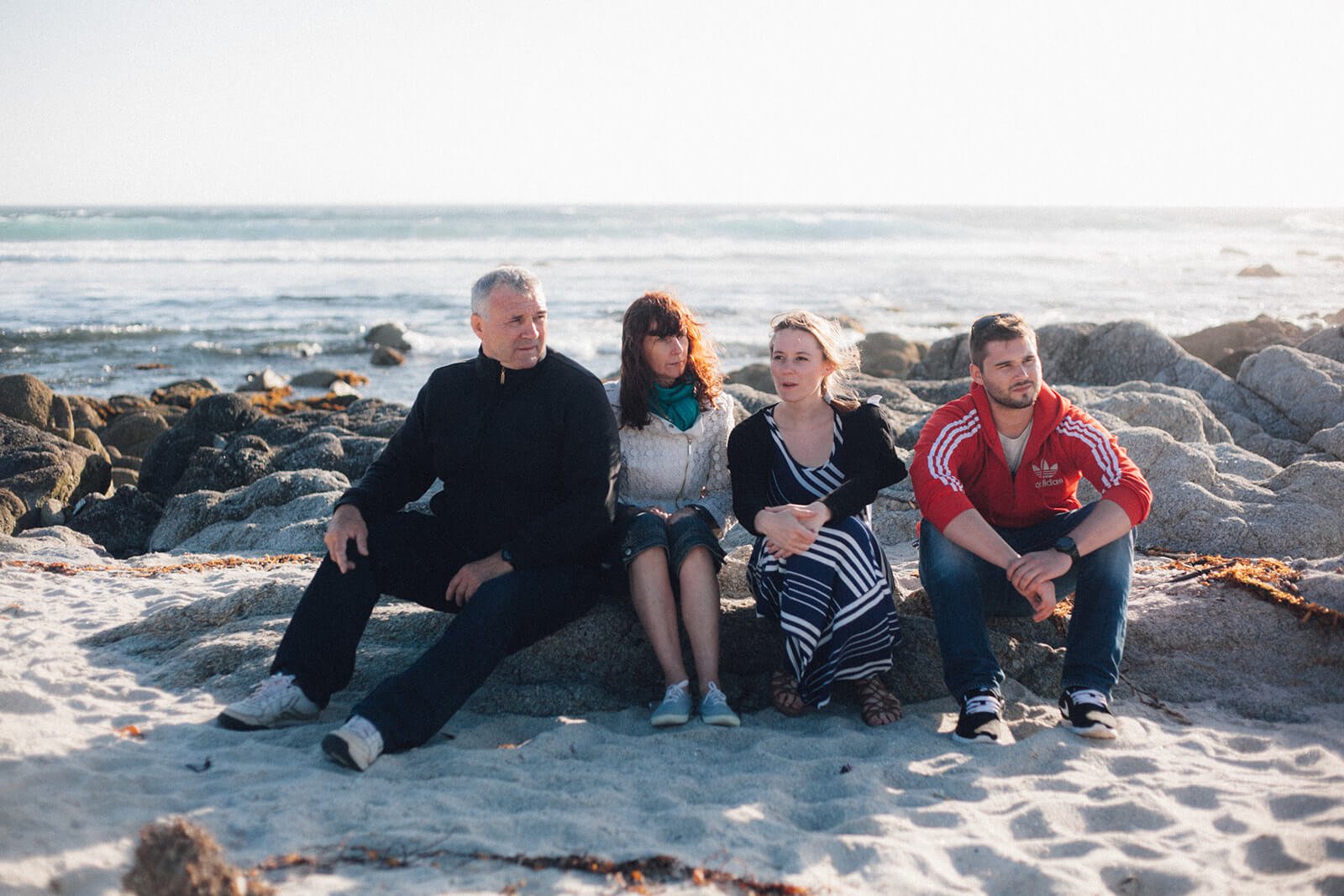 Family of four sitting on rocks on the beach in front of the ocean